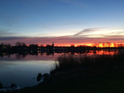 Sonnenuntergang über der ruhigen Treene, reflektierende Farben am Himmel.