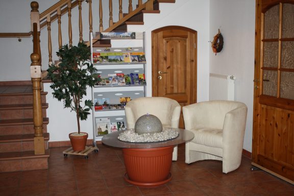 Heller Flur mit Treppe, zwei weißen Sesseln, einem Tisch und Pflanzen.