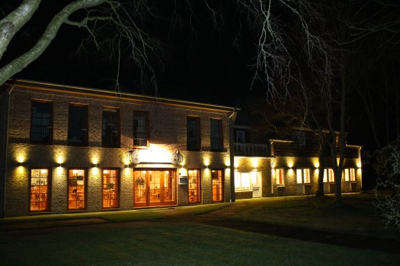 Beleuchtetes Gebäude bei Nacht mit Bäumen im Vordergrund.